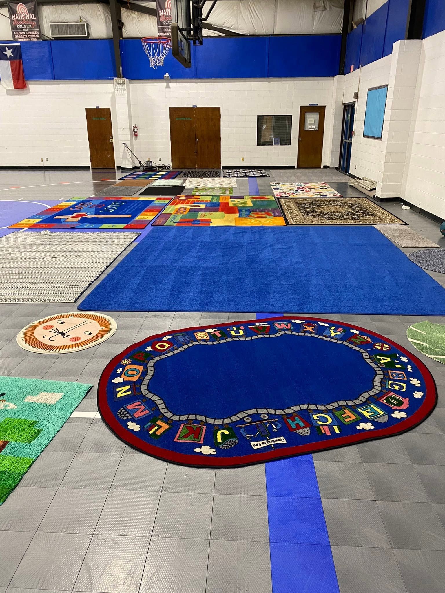Gym with colorful classroom rugs and mats arranged on the floor under basketball hoops.