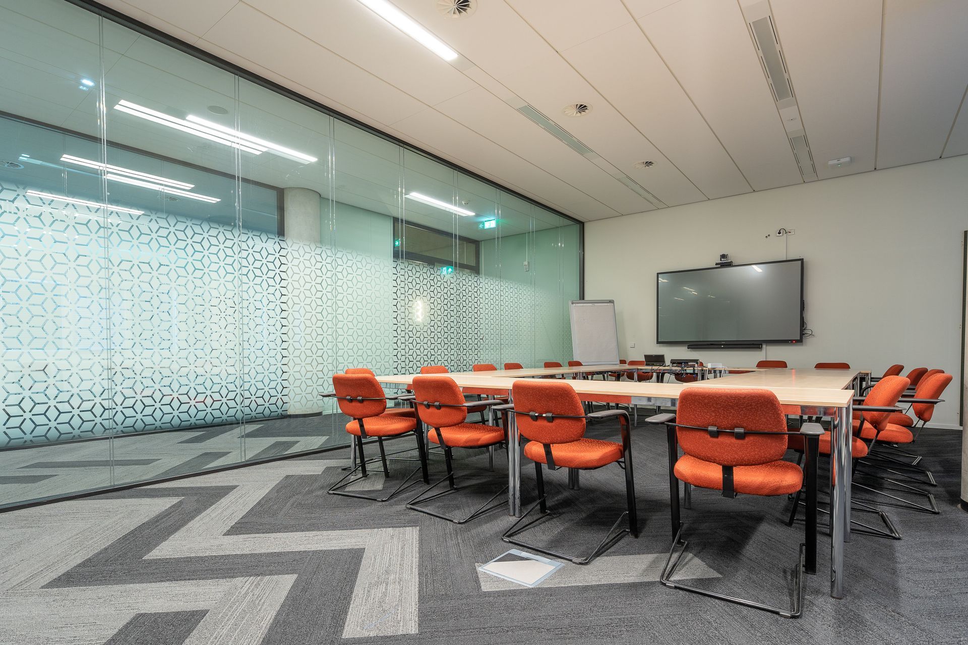 Modern conference room with orange chairs, a large table, and a wall-mounted display on a glass-walled side.