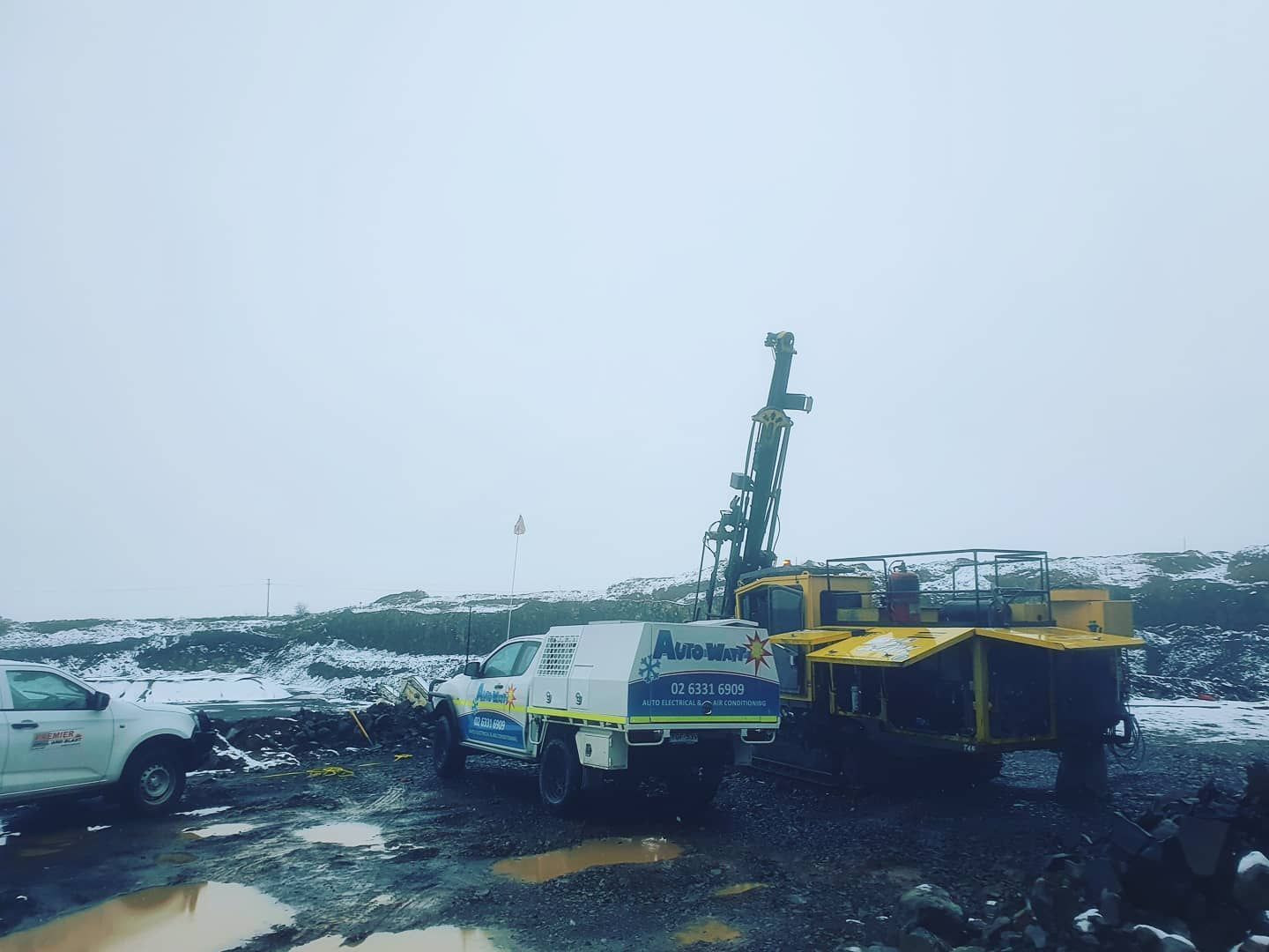 A Yellow Drilling Machine and White Truck on a Snowy, Muddy Worksite — Auto Watt in Kelso, NSW