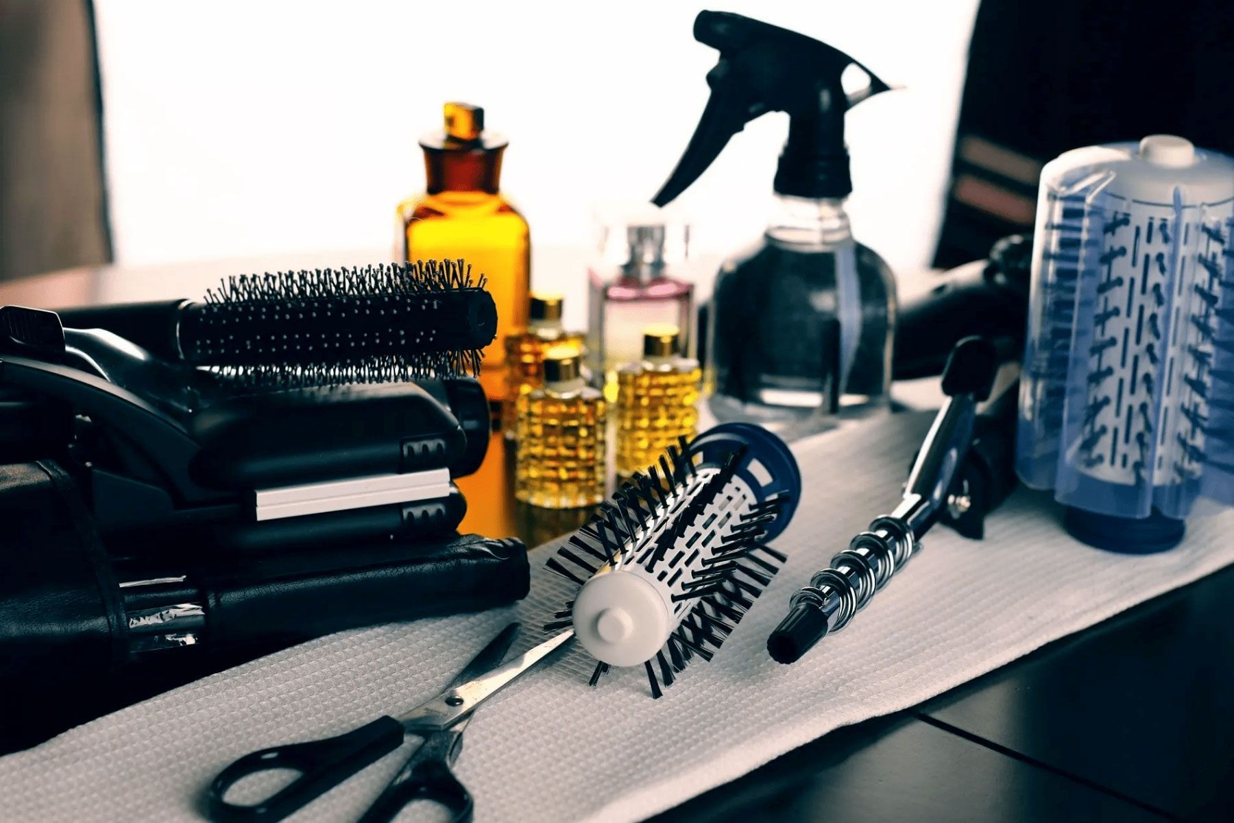 Strumenti e prodotti per lo styling dei capelli su un bancone di un salone, tra cui spazzole, flaconi spray e articoli per la cura della persona.