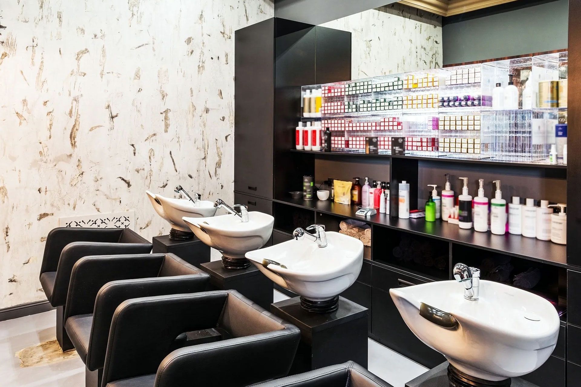 Salone da parrucchiere moderno con poltrone da styling nere, lavabi e scaffali per i prodotti.