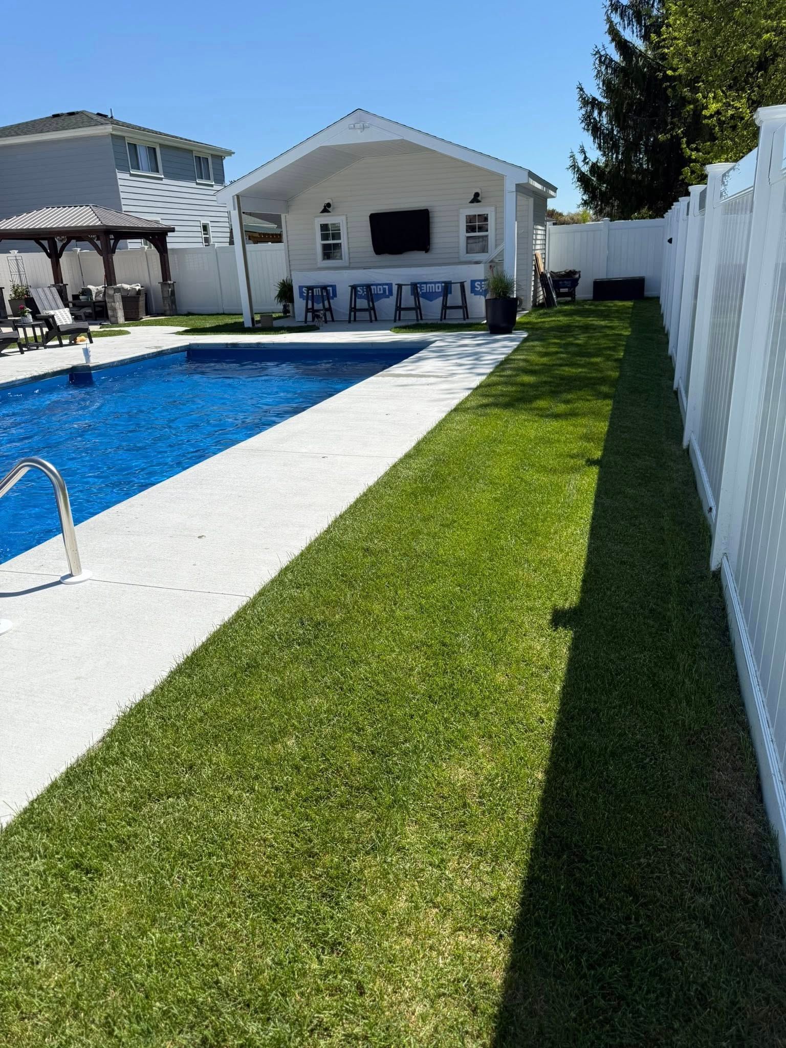 Poolside bar with blue pool, green grass, white fence, and blue chairs.