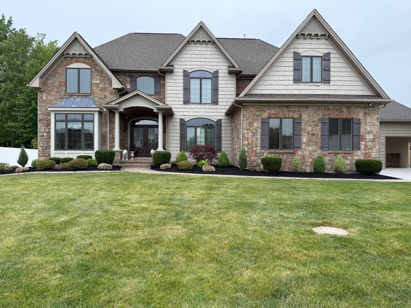 Two-story house with brick and siding, multiple gables, dark shutters, manicured lawn.