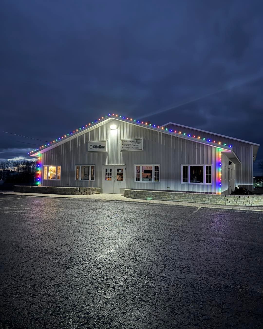 Building with Christmas lights at dusk. Metal siding, glass windows, dark sky.