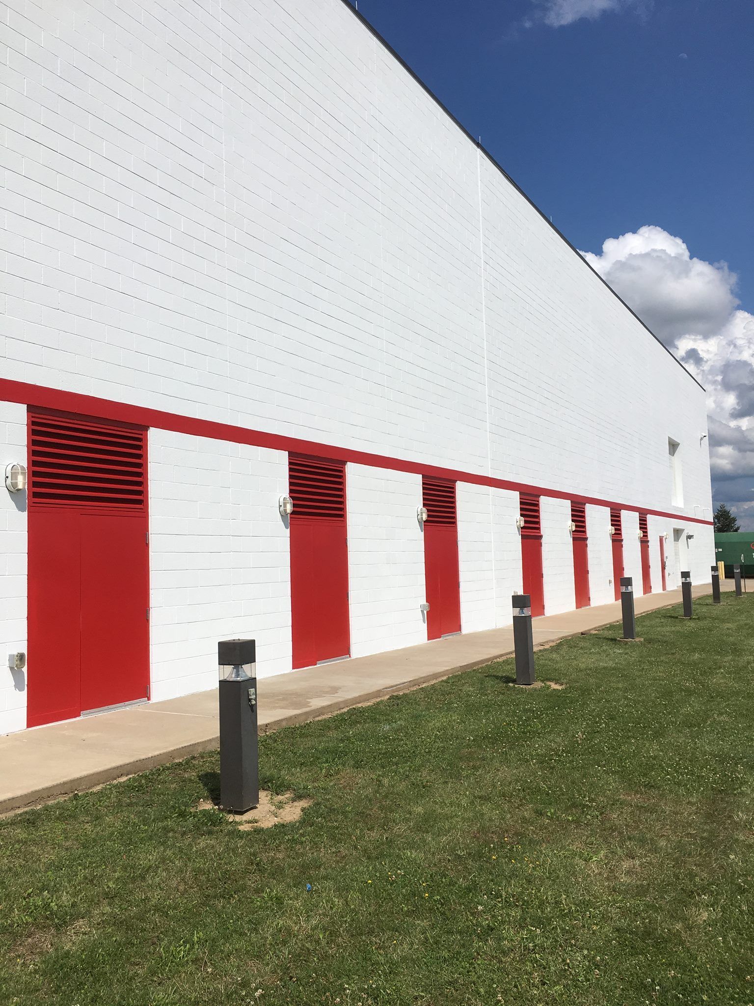 Modern white building with red vertical accents and small windows on a grassy slope under a blue sky