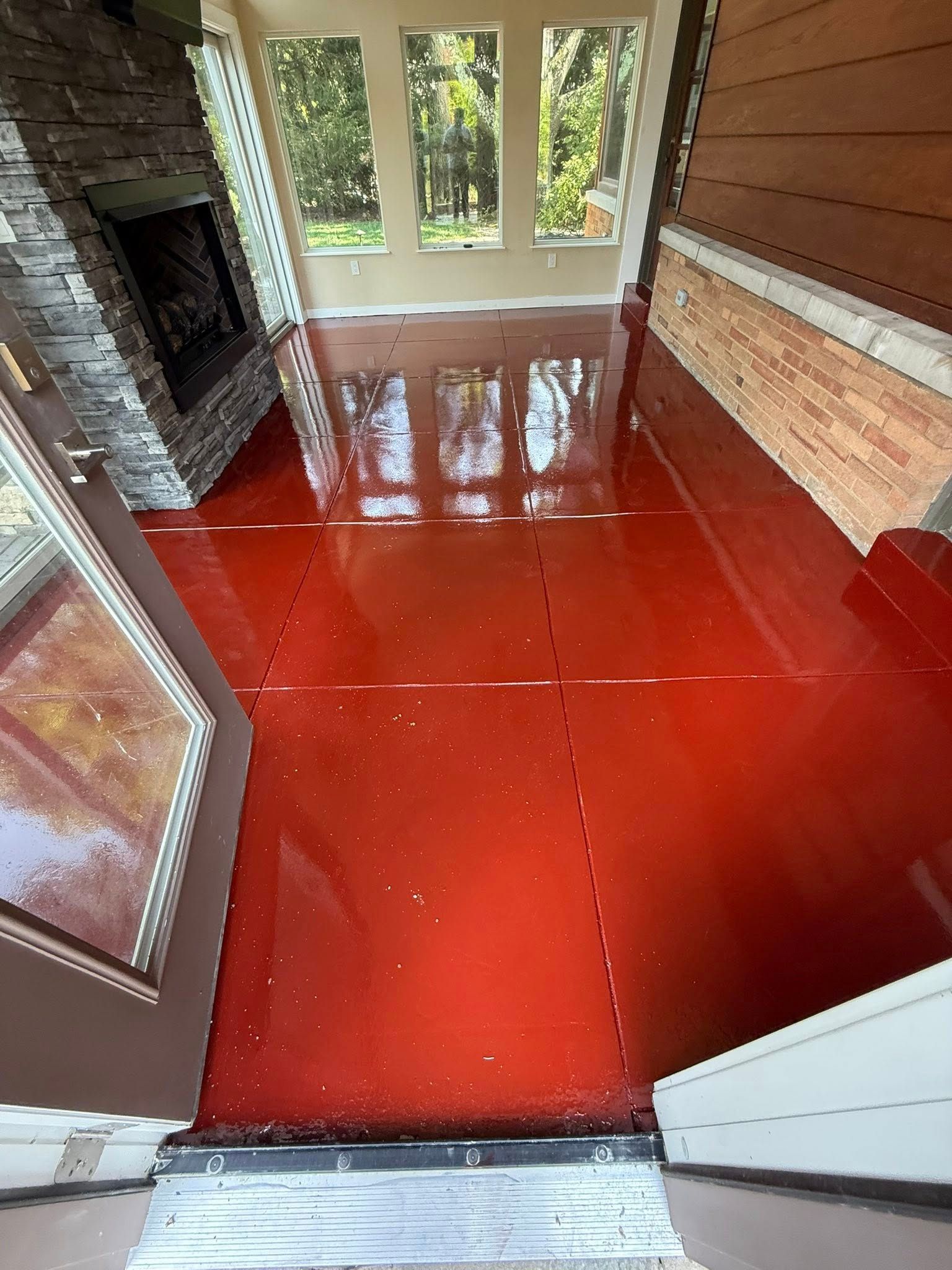 Red glossy floor in a bright sunroom with large windows and stone fireplace.