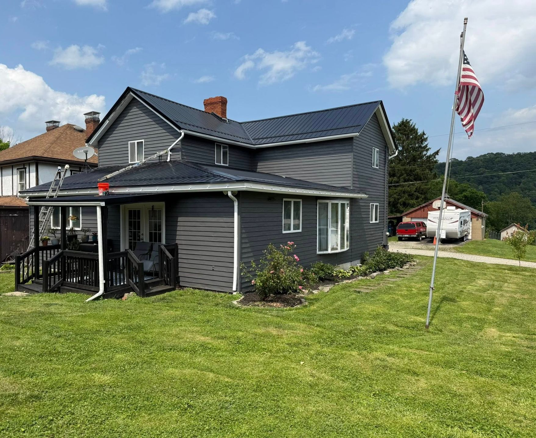Gray two-story house with porch, black roof, green lawn, and an American flag in front.