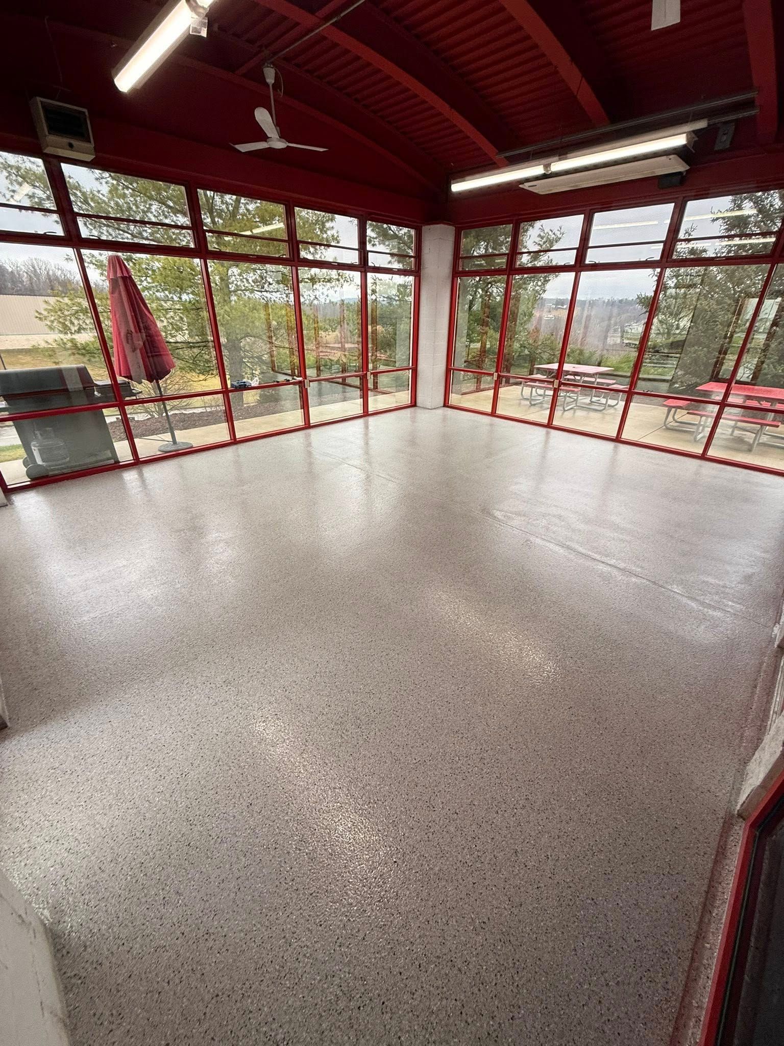 Empty red-framed room with large windows, polished floor, and a view of trees outside