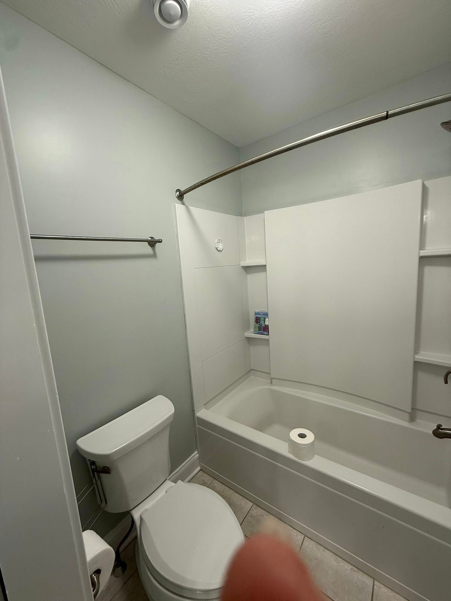 Accessible bathroom with toilet, shower-tub combo, and grab bars in a small white restroom