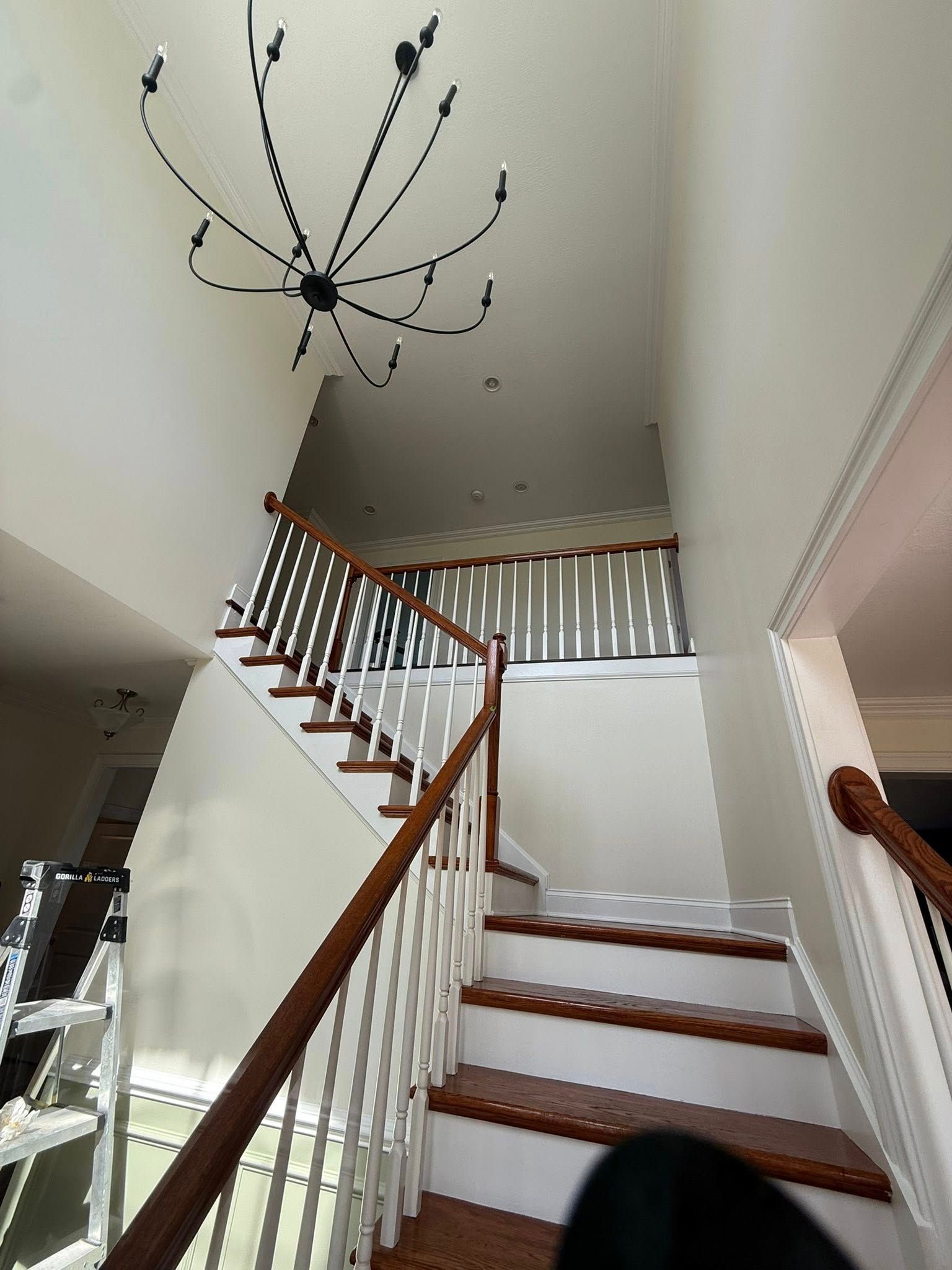 White staircase with wooden handrails in a bright foyer and a modern chandelier overhead