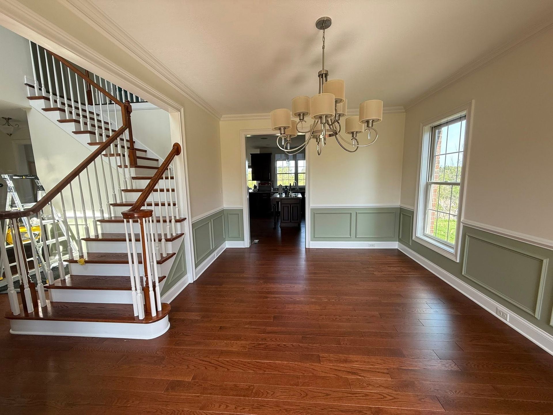 Bright entry hall with hardwood floors, staircase, chandelier, and windows with green wainscoting.
