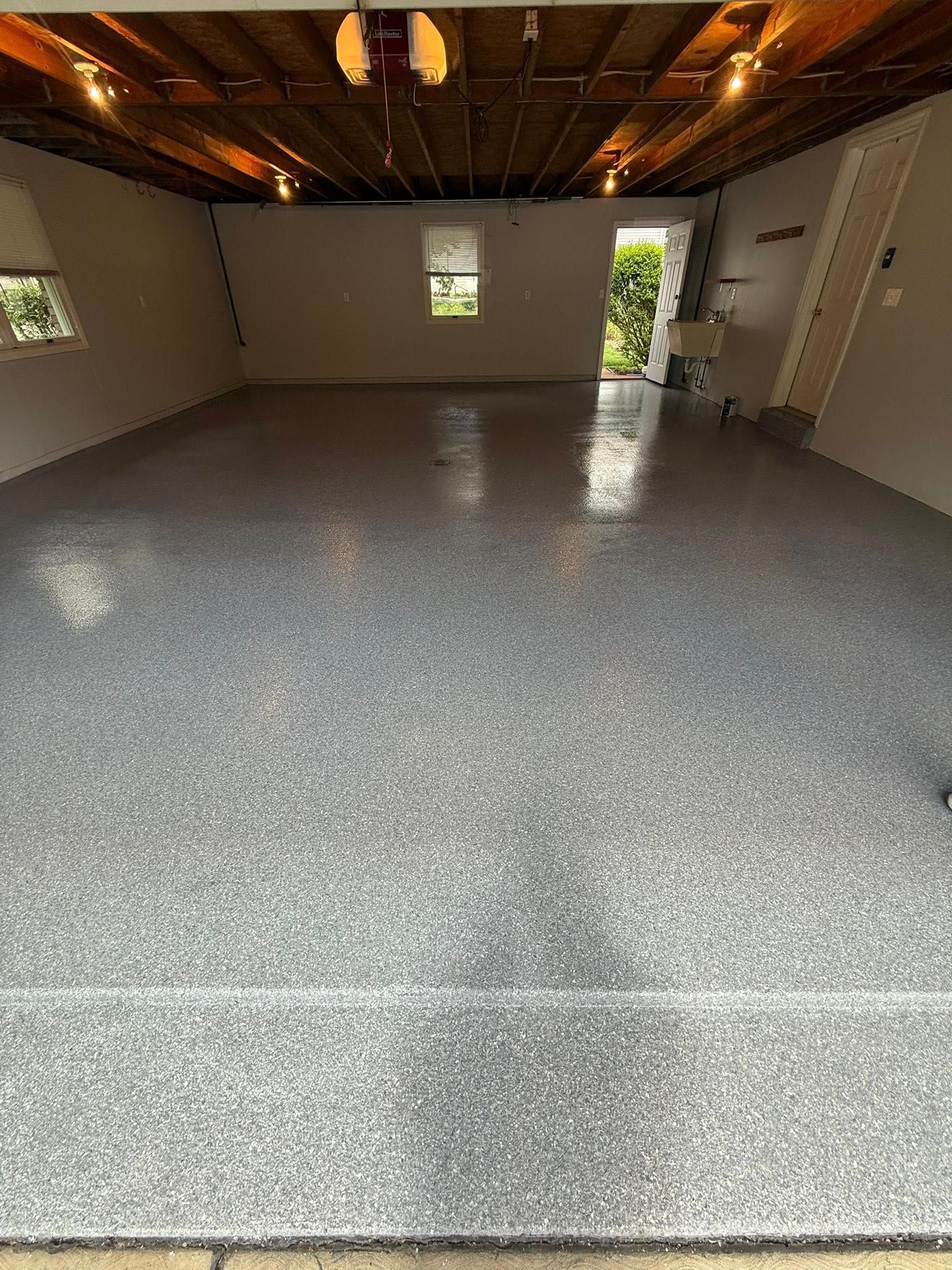 Empty unfinished room with gray epoxy floor, exposed ceiling, and daylight from an open doorway.