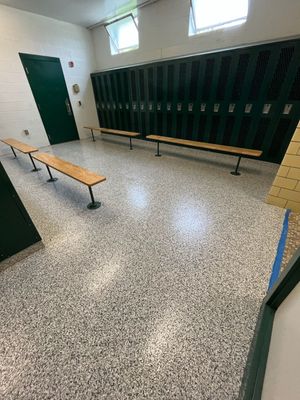 Empty school locker room with green lockers, benches, and speckled tile floor