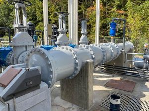 Large gray industrial pipeline and valves outdoors with autumn trees in the background