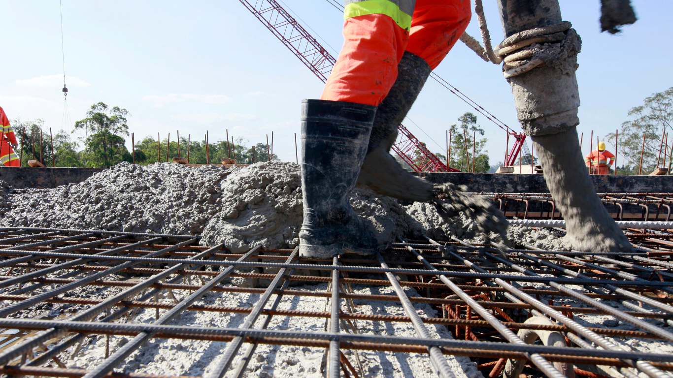 Construction workers standing on rebar at a concrete foundation site with gravel and a crane in the background