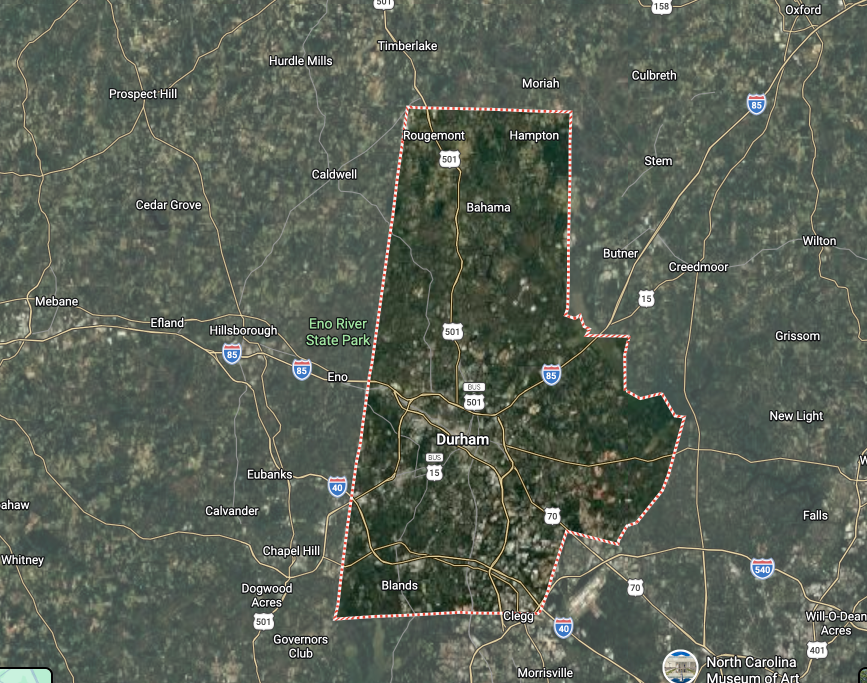 Satellite map with a pink-outlined county or district boundary over a green rural landscape.