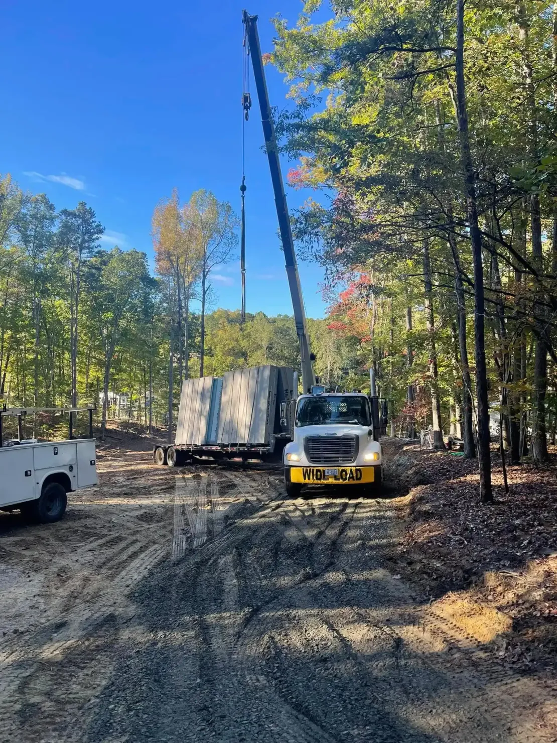 Truck and crane lifting a panel in a wooded dirt clearing under a blue sky