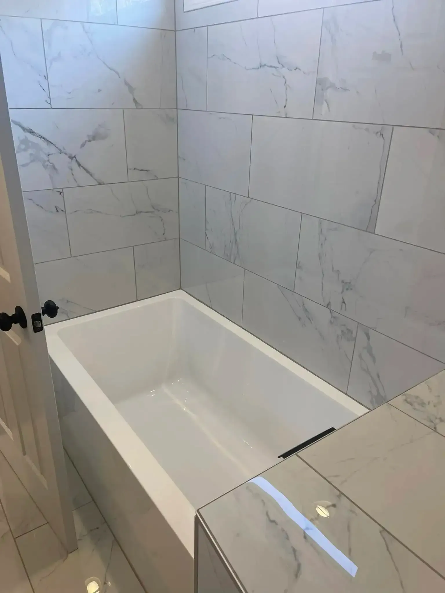 Modern tiled bathroom with a white bathtub and glass shower screen