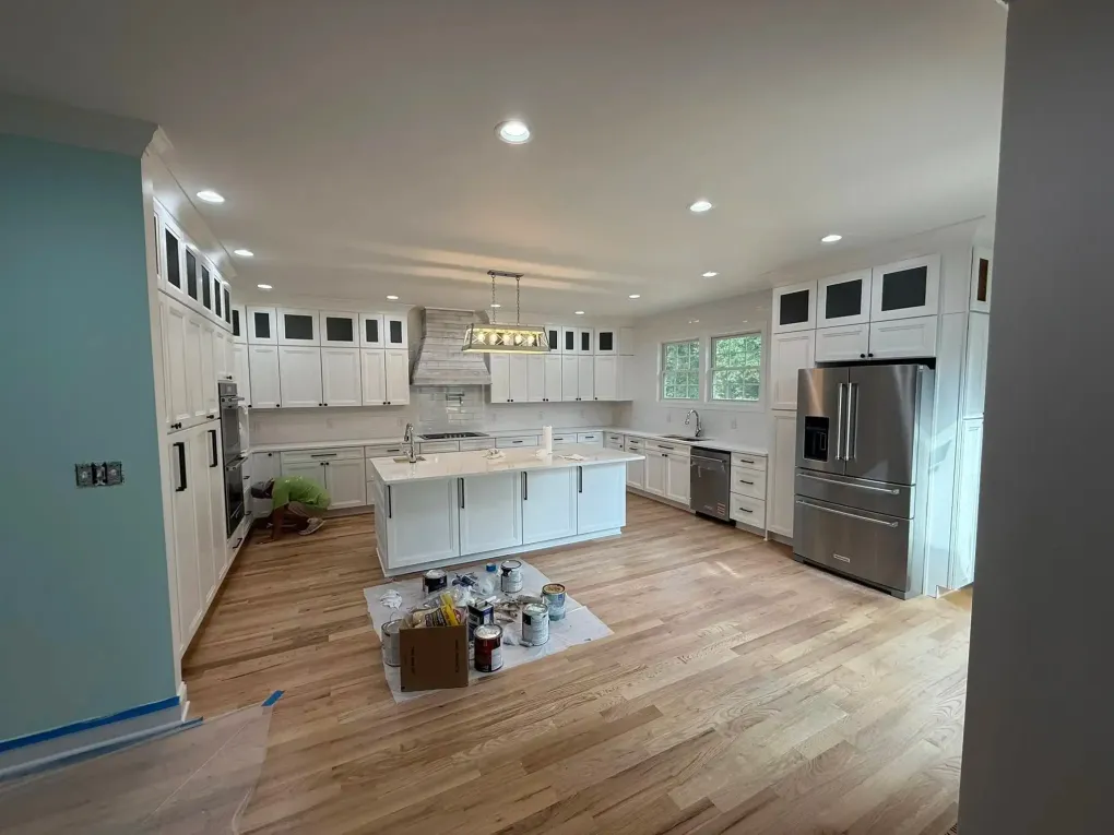 Bright modern kitchen with white cabinets, island, stainless fridge, and wood floors
