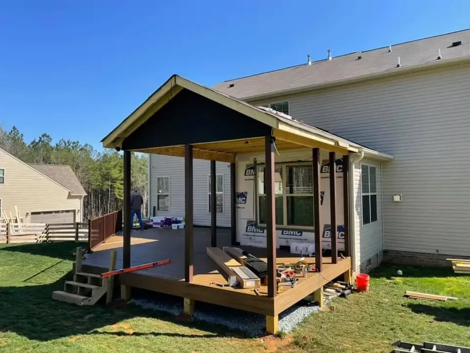 Covered wooden deck ramp beside a beige house, with railings and steps in a sunny yard.