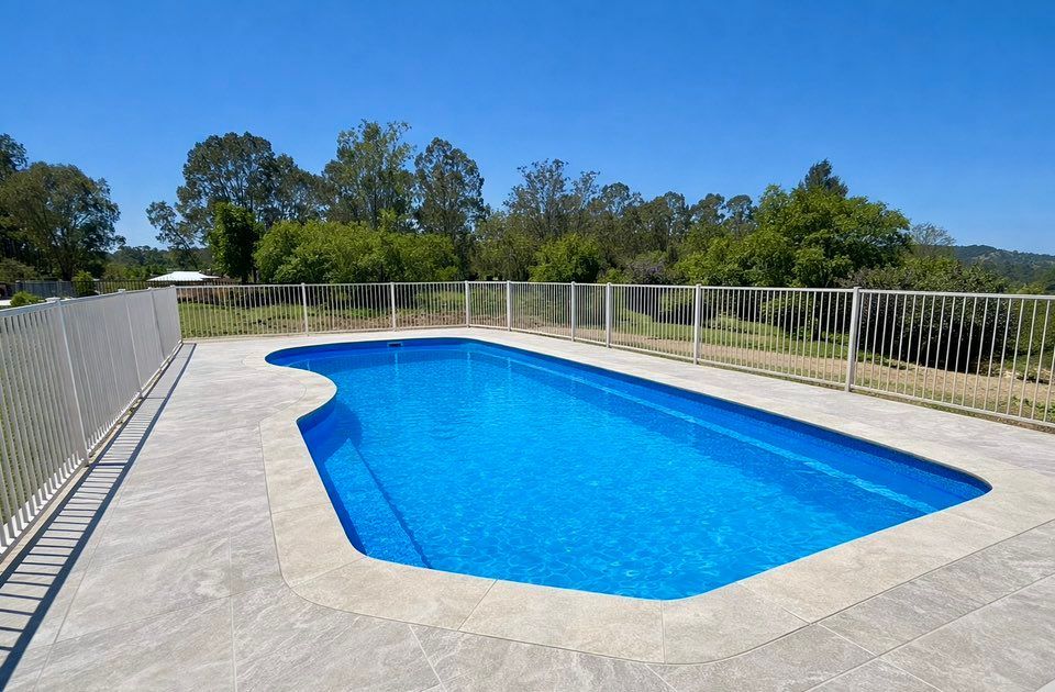 Aerial view of two people swimming in a rectangular backyard pool surrounded by patio and grass.