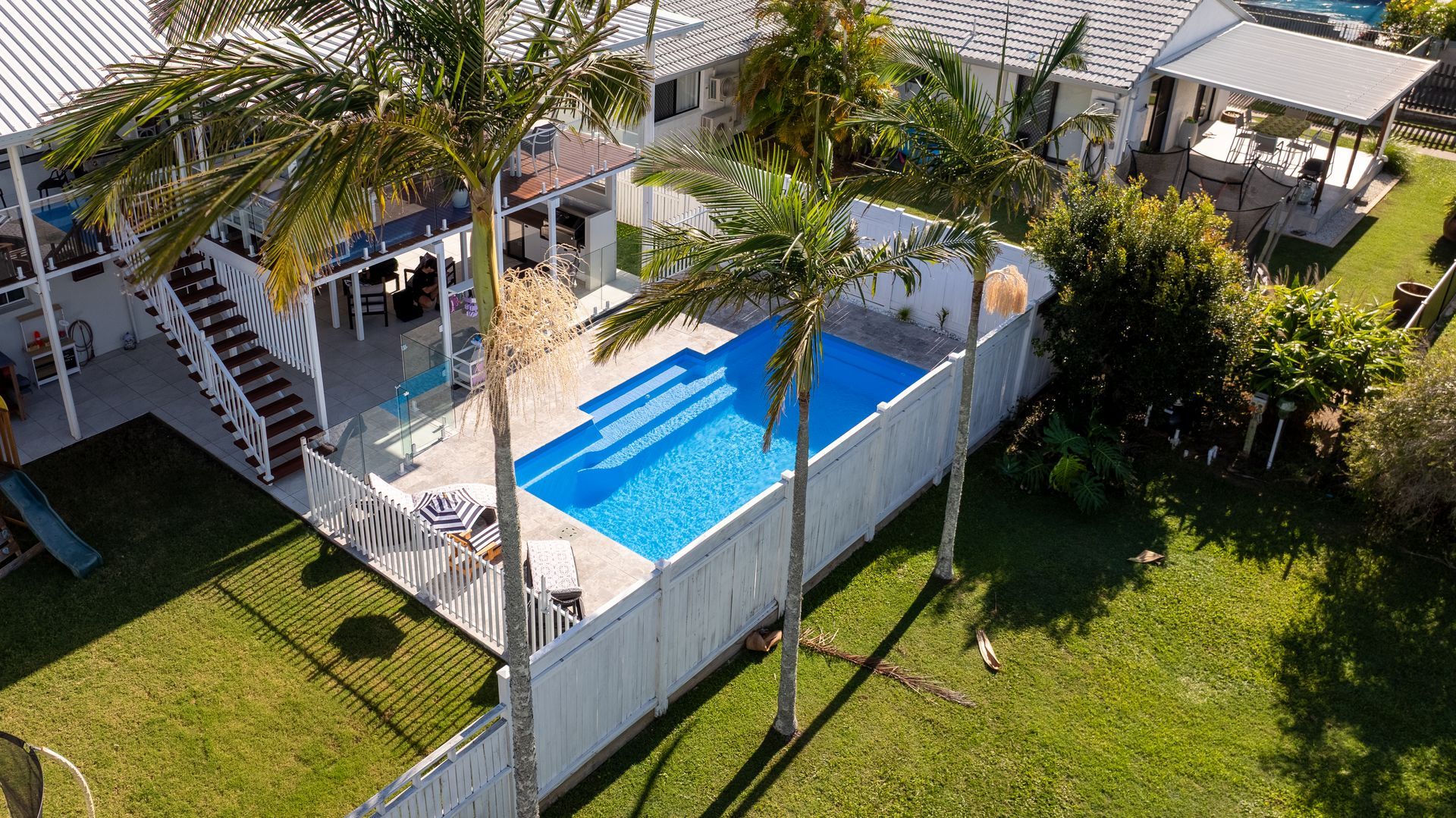 Blue rectangular swimming pool with tiled water and a light stone deck beside it.