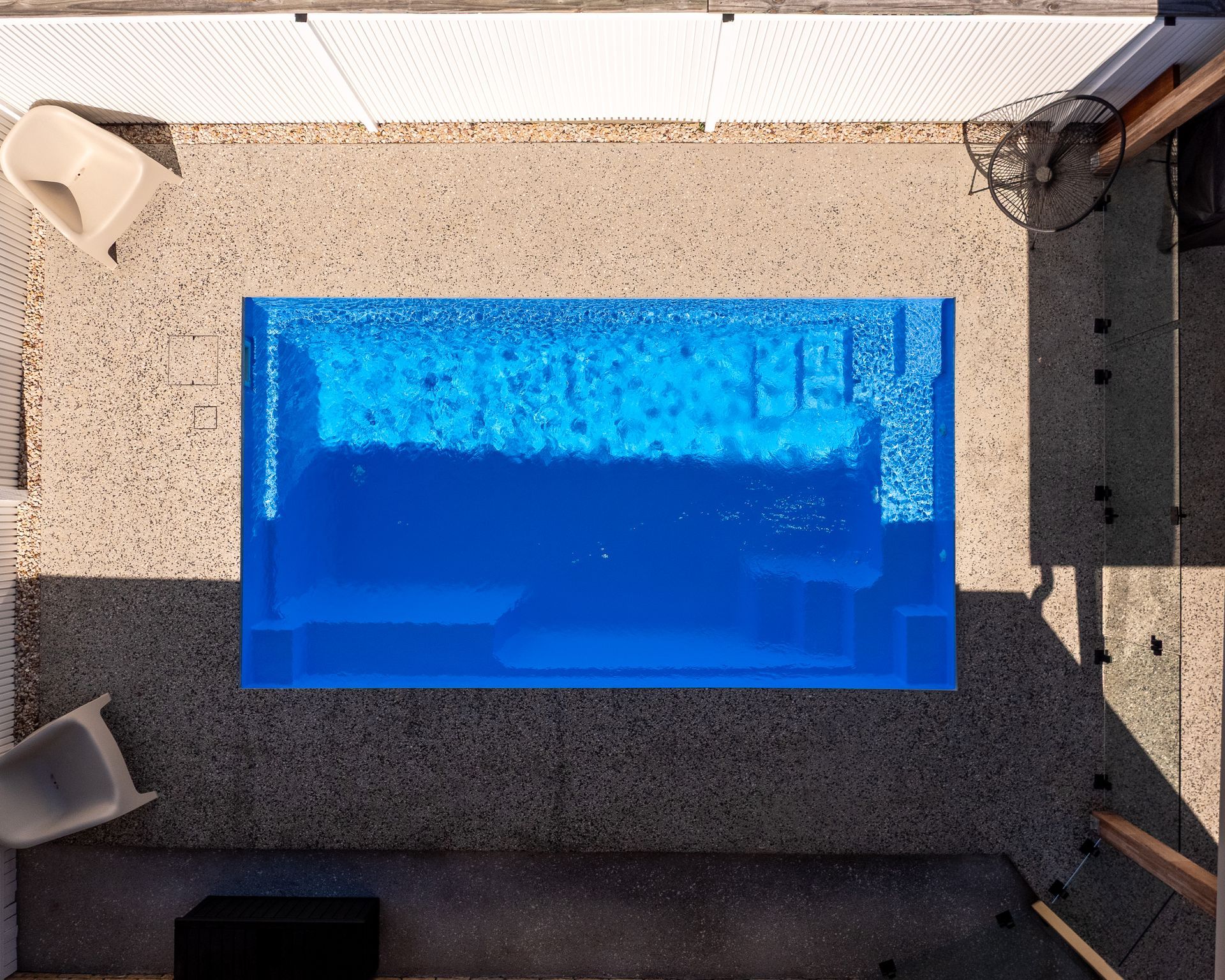 Poolside patio with black chairs and white lounge chairs beside a turquoise swimming pool.