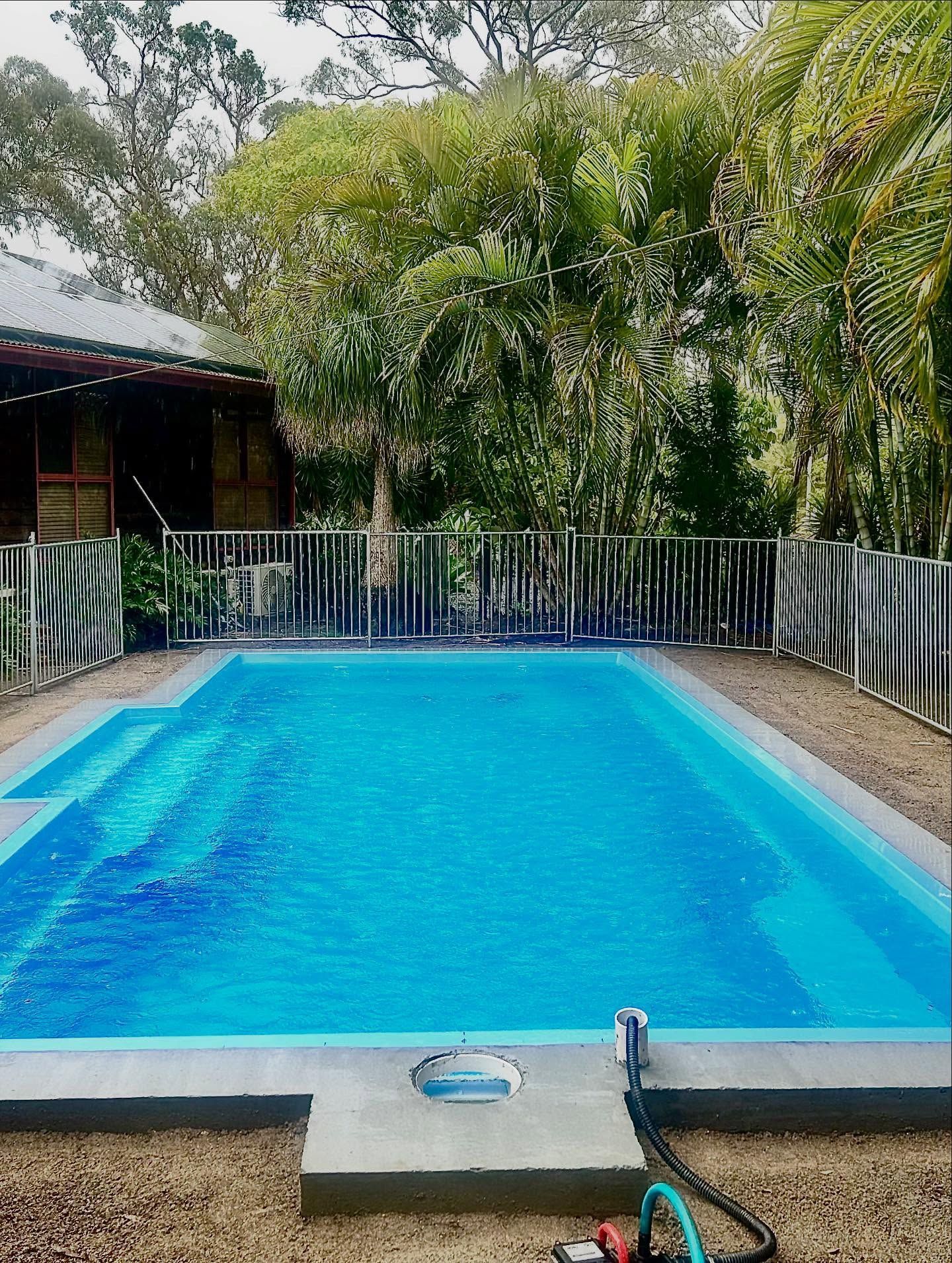 Outdoor lap pool with turquoise water under a cloudy blue sky, beside a outdoor area 