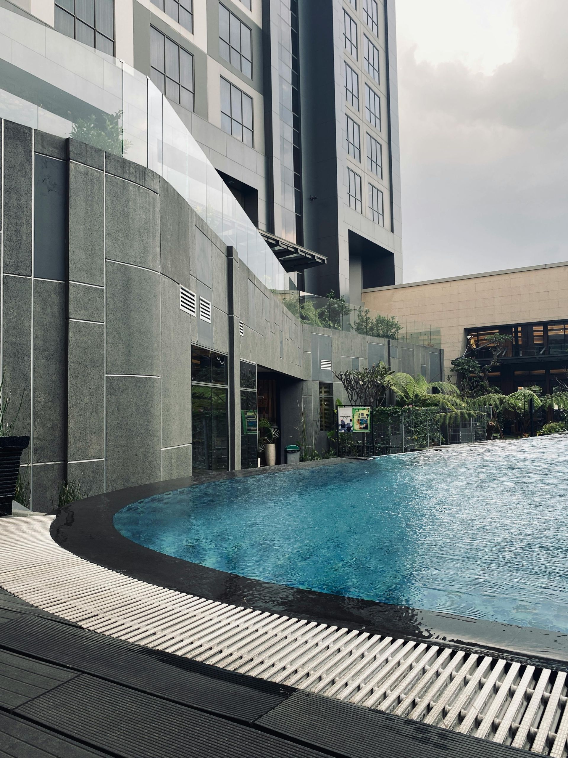 Curved rooftop pool beside a modern high-rise building, with water and lounge deck area