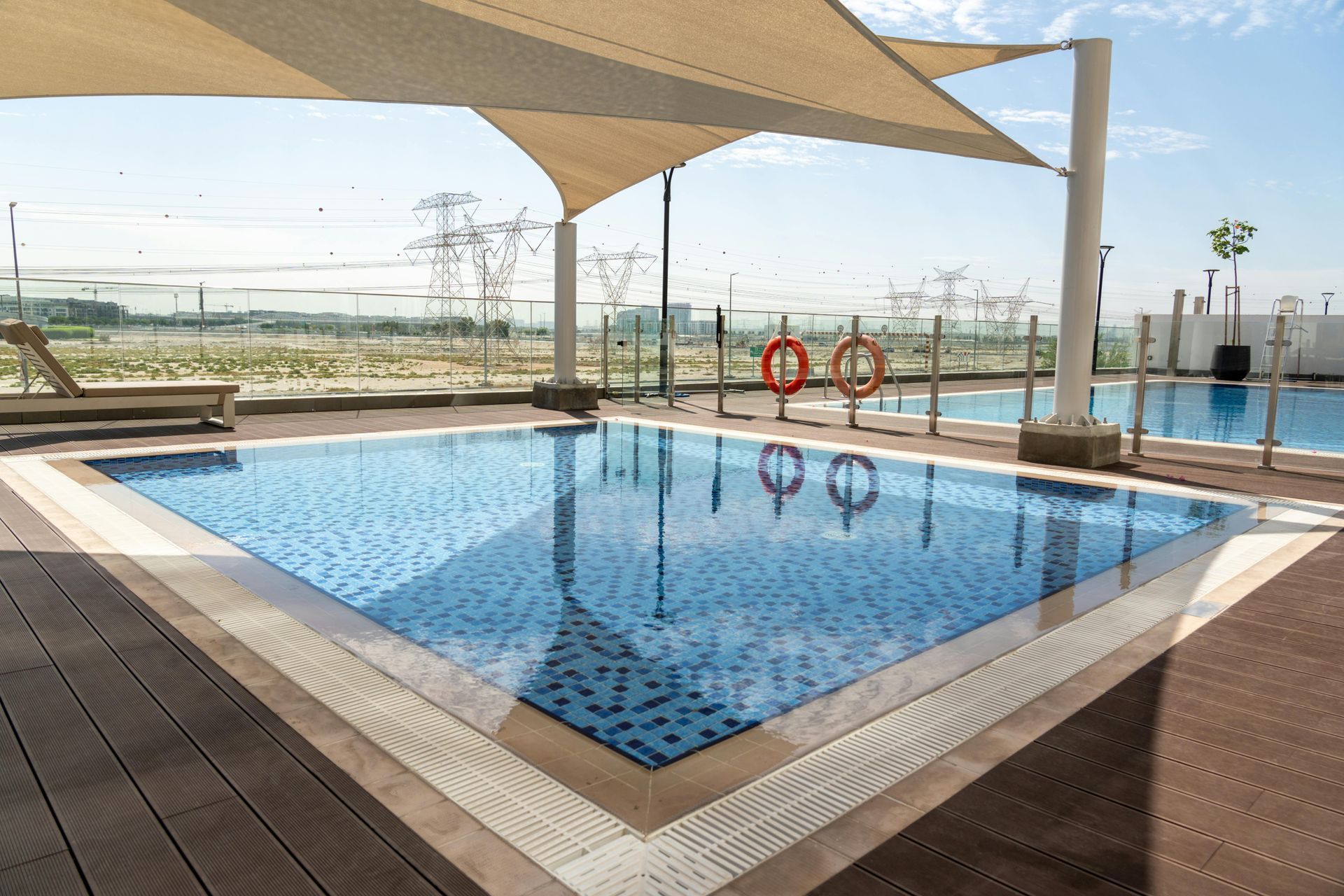 Rooftop pool with blue water, tan sun shade, and lifebuoys overlooking a distant city skyline