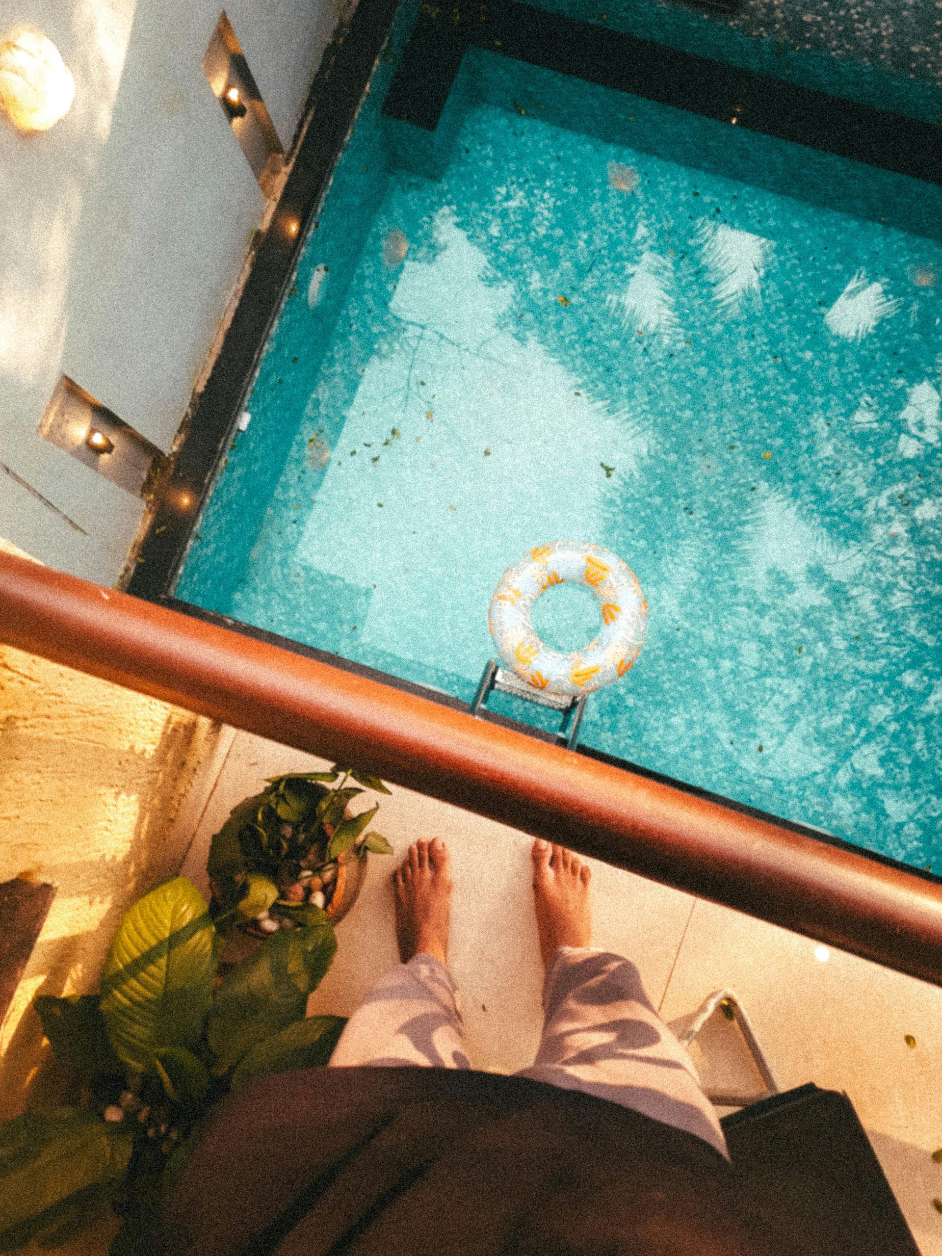 Person standing on a balcony overlooking a turquoise pool with a yellow float ring