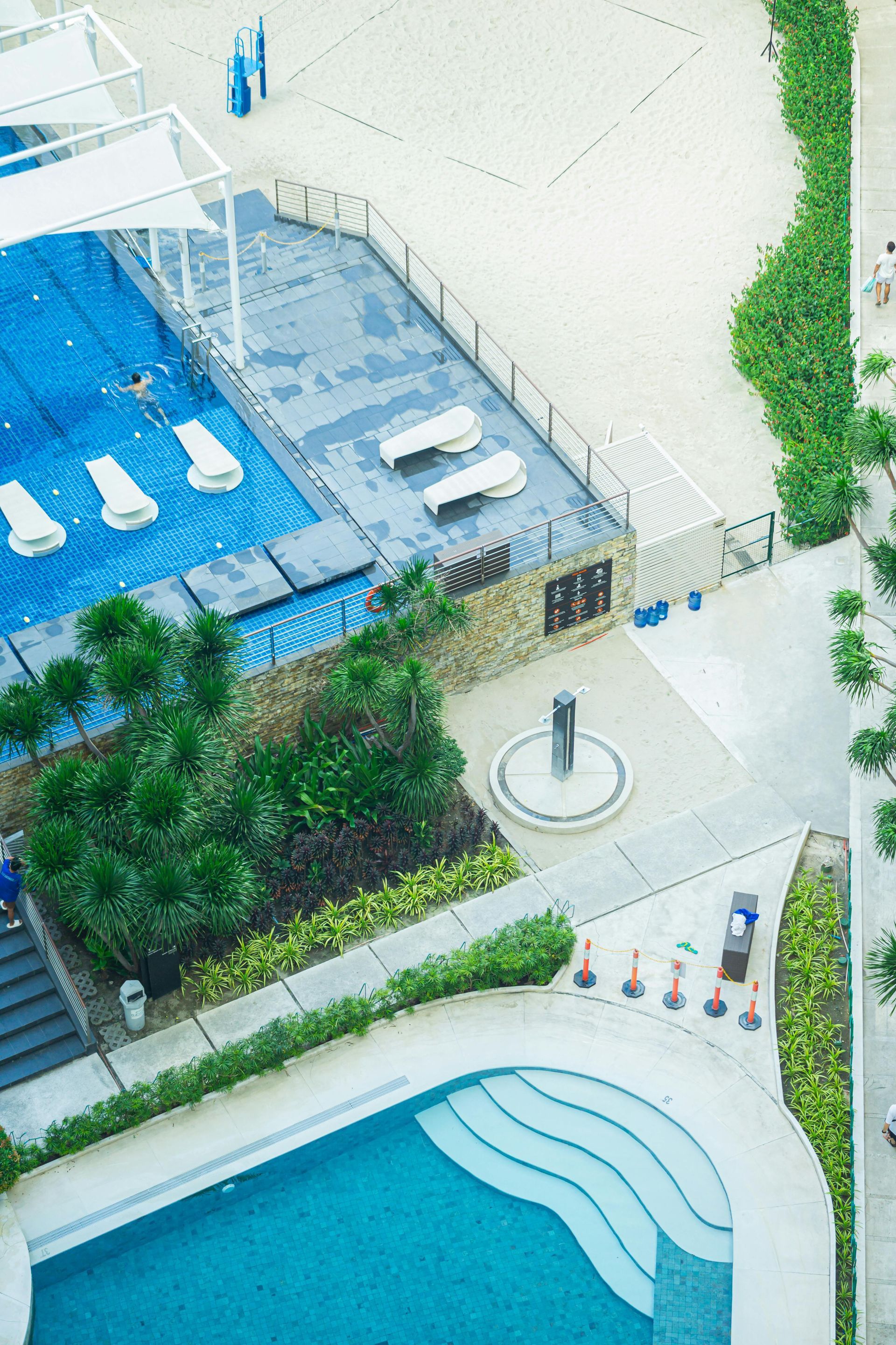 Aerial view of a resort pool, lounge chairs, and landscaped walkway beside a building.