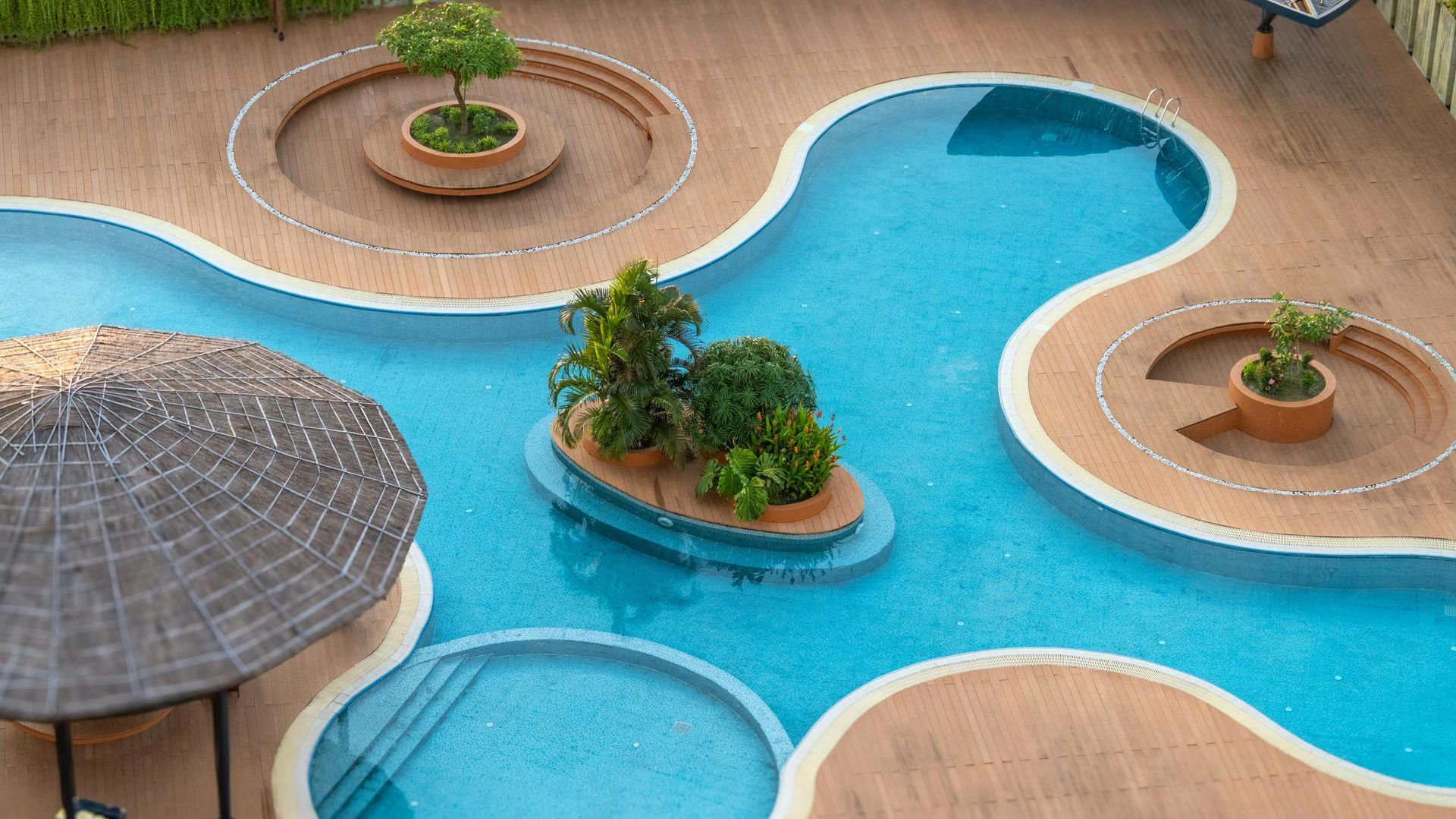 Curved blue pool with small island planters and tan deck, viewed from above