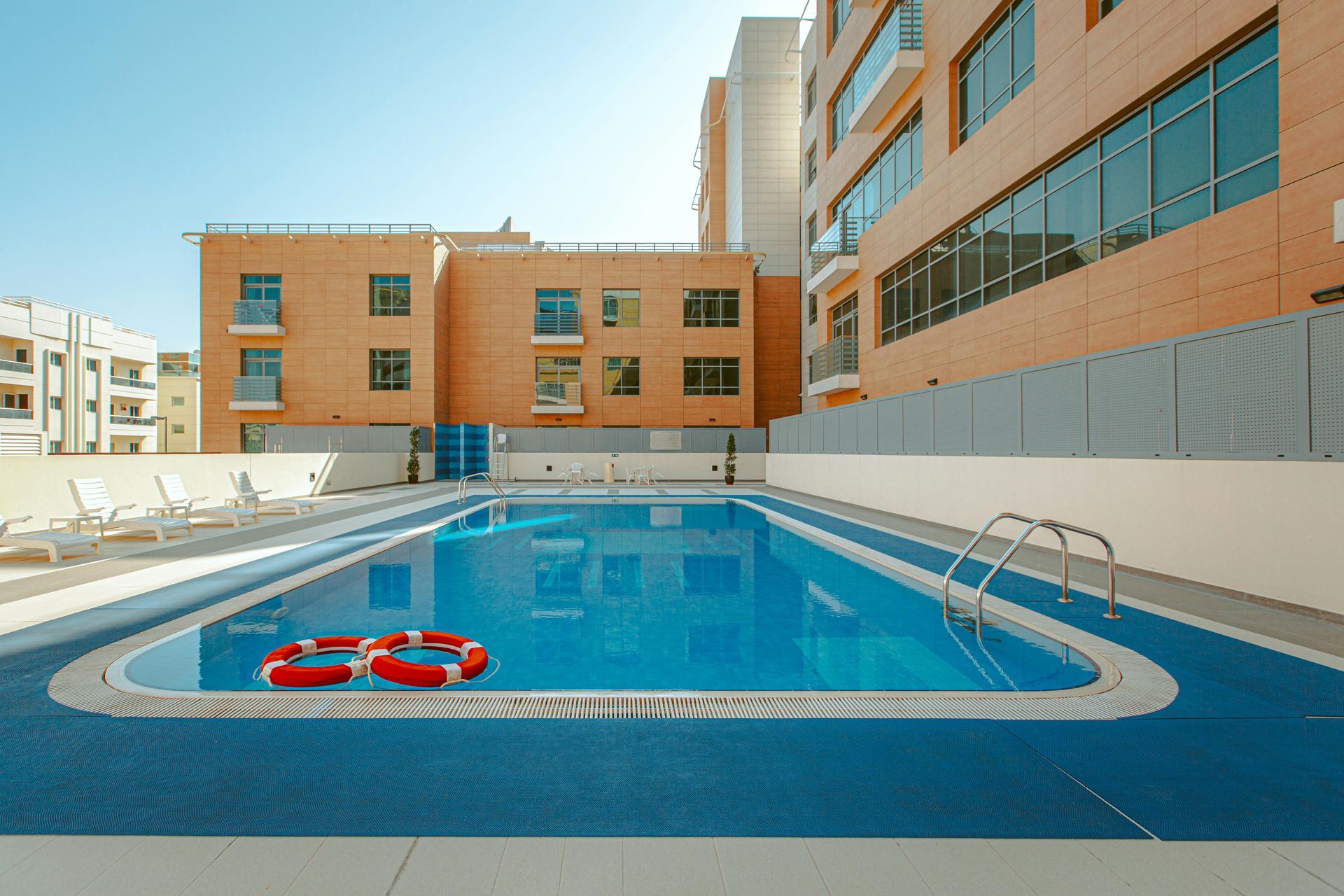 Rooftop pool with clear blue water, red-and-white lifebuoy, and surrounding tan apartment buildings
