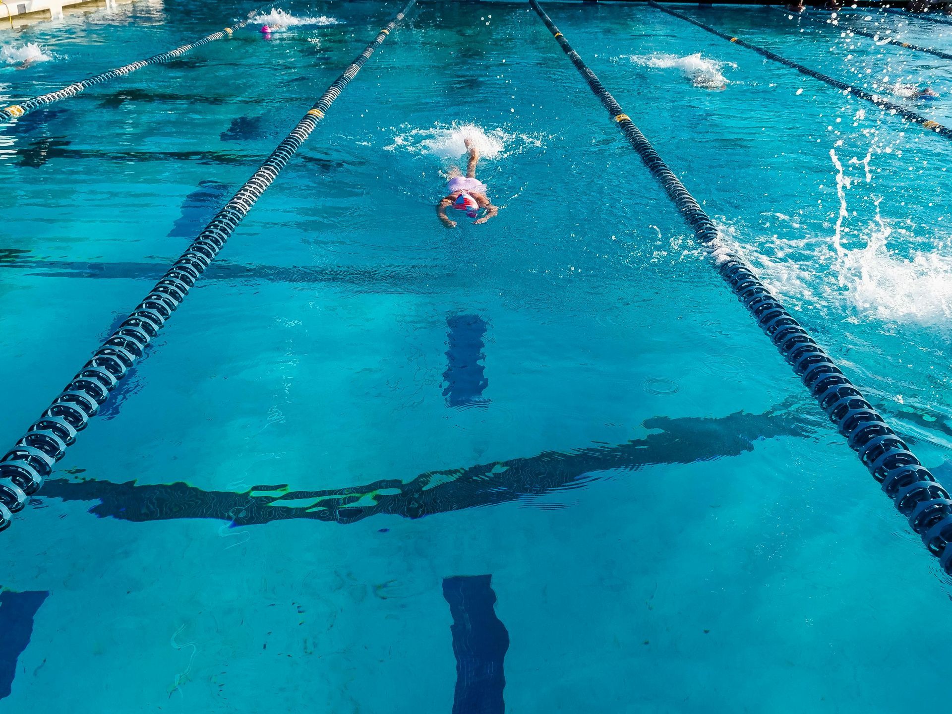 Swimmer in red cap racing in a turquoise indoor pool lane, seen from above
