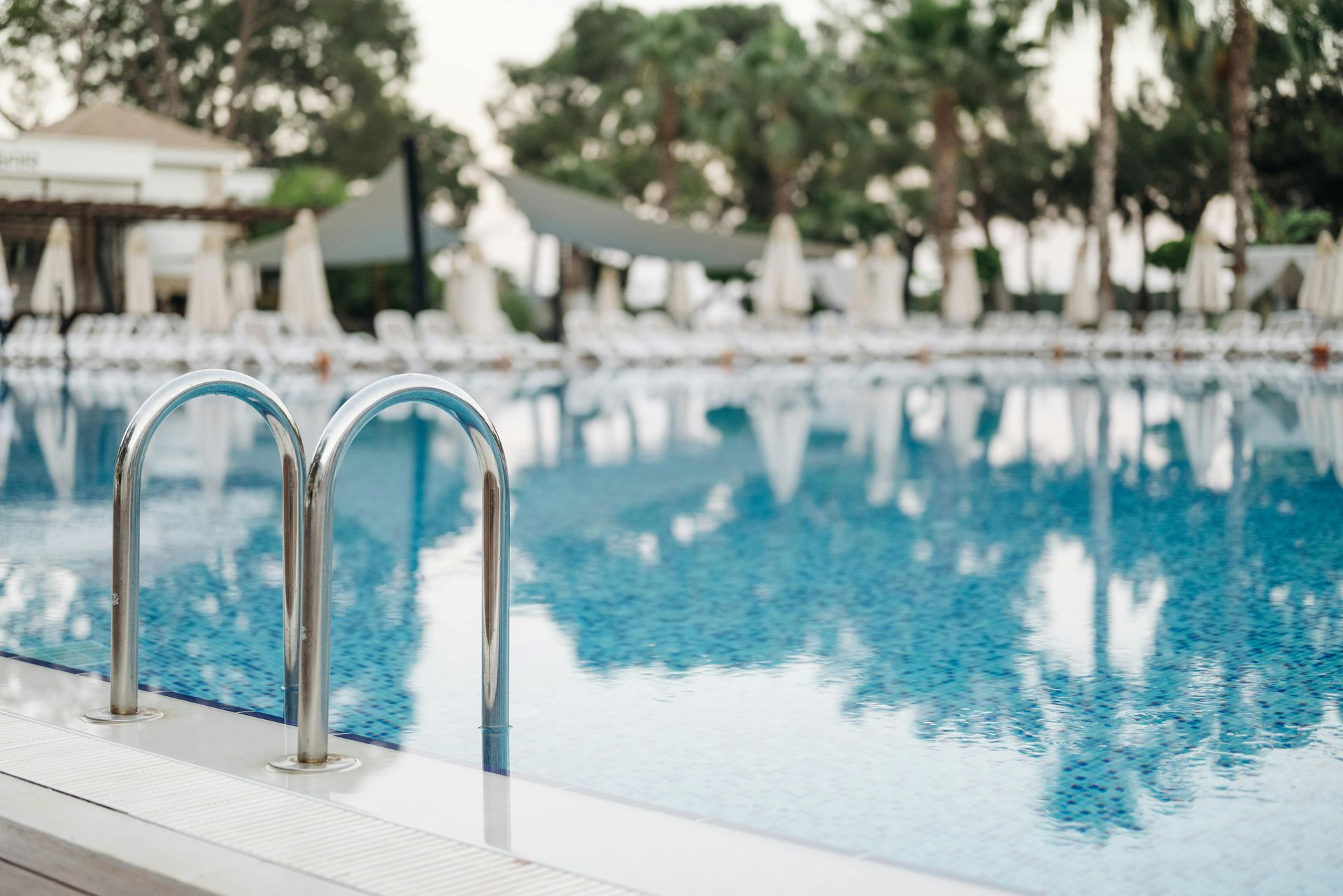 Outdoor swimming pool with metal ladder, turquoise water, and white lounge chairs under trees