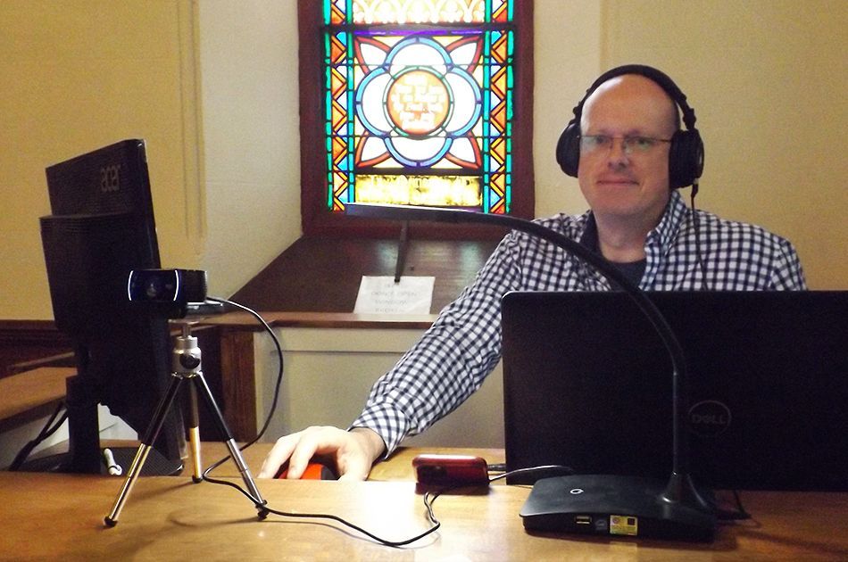 Man wearing headphones sits at Tech Team's desk with a laptop open in front of a stained-glass window
