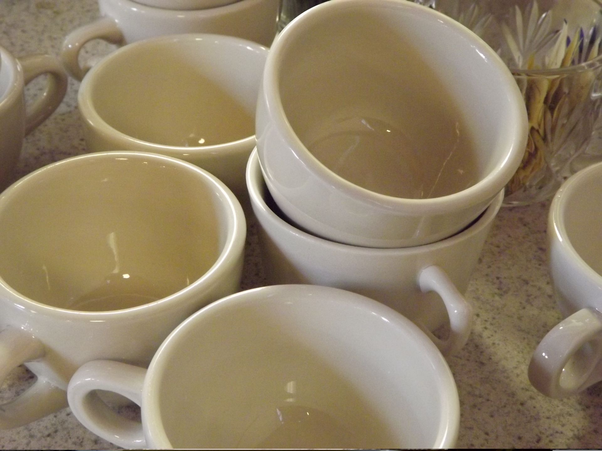 A cluster of cream-colored ceramic mugs are stacked on a countertop.