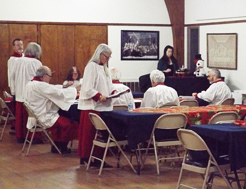 Music Ministry members sit at tables in the Parish Halll, garbed in red & white gowns, preparing for worship service.