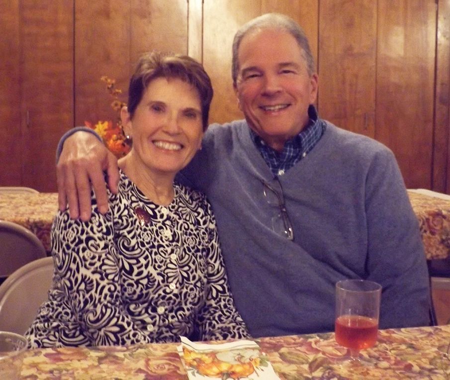 A smiling couple sits close together at a table in the Parish Hall, w/wood-paneled doors in the background.