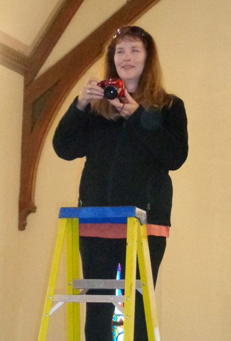 Digital Director is standing on a step ladder in the sanctuary, holding a camera & preparing to take a group photograph.