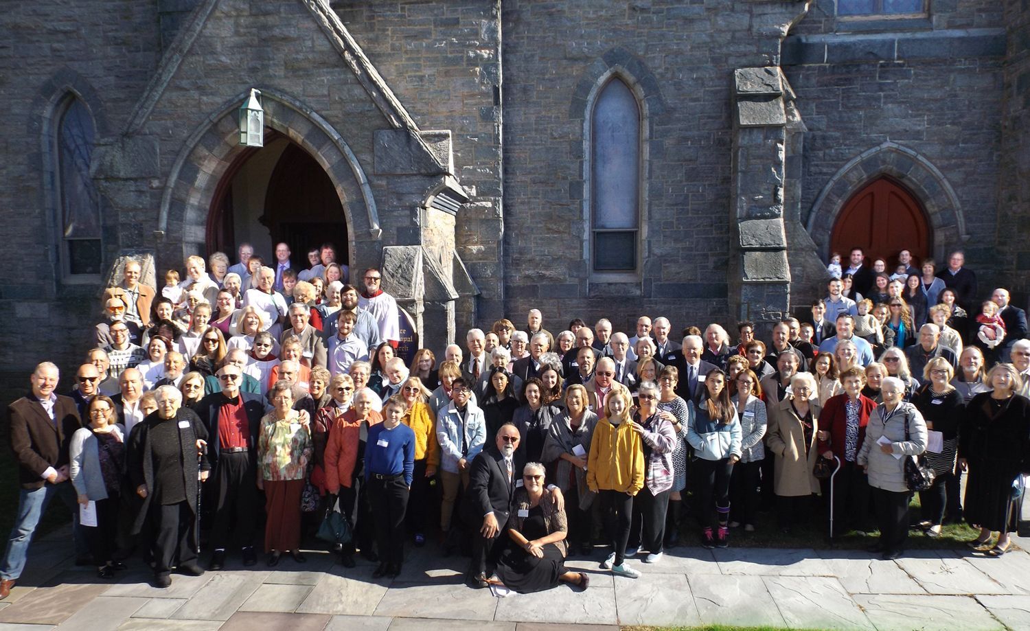 The Congregation poses together outdoors on Grace Church's stone front steps in bright sunlight