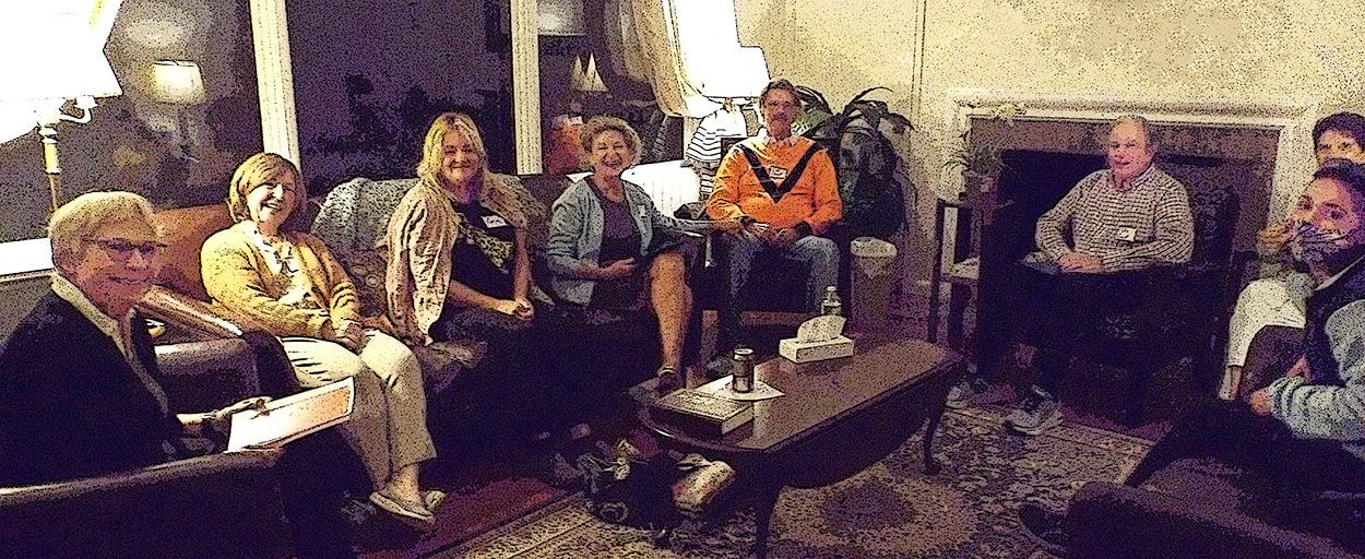 Small group seated for a break-out session, on upholstered furniture atop an Oriental rug, in the dimly lit Hudson Room