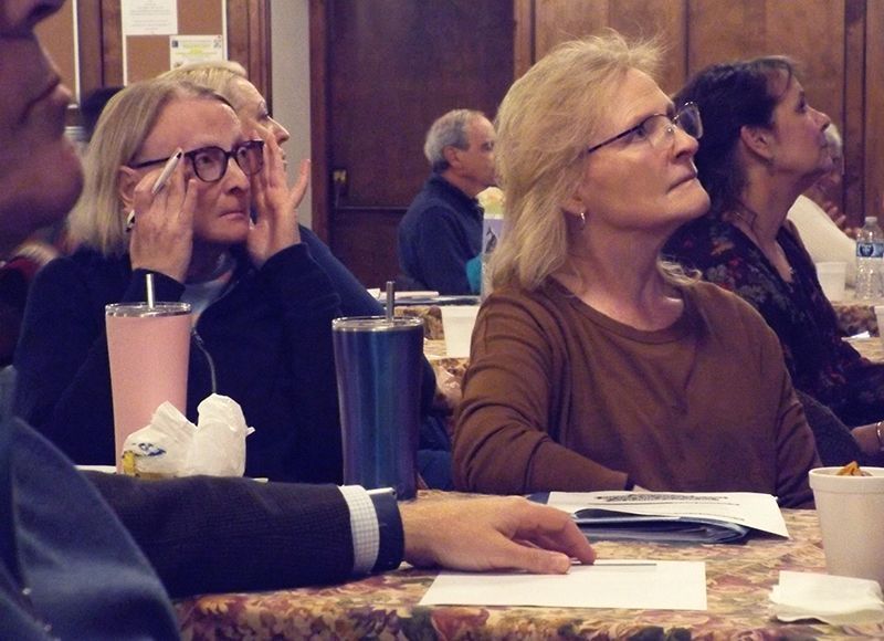 Two women sit at a table, listening to a lecture in the Parish Hall.