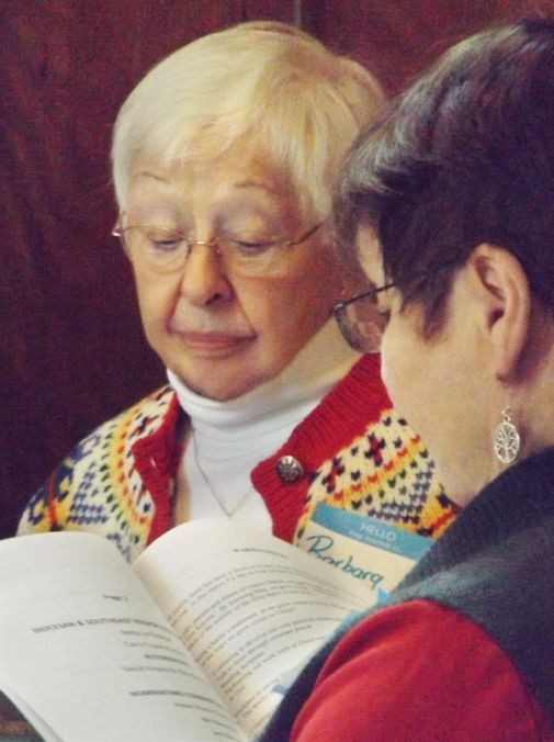 Two women in glasses look down to examine some hardcopy handouts together