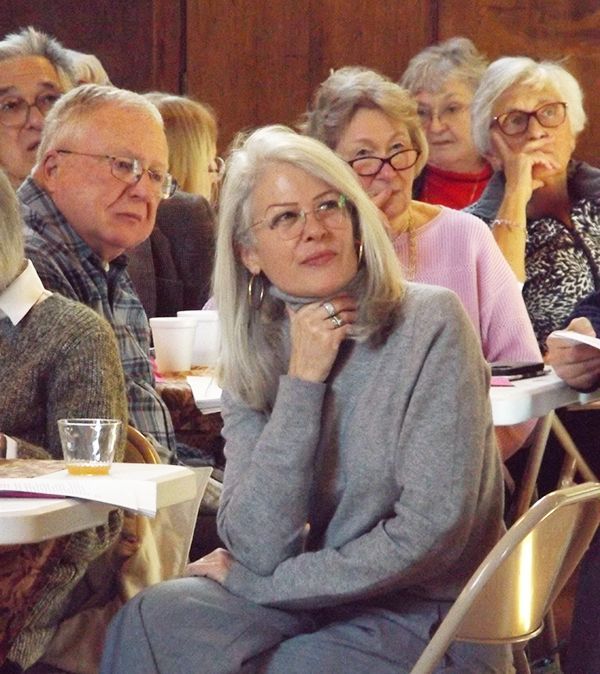 A group of parishioners sits at tables together in the Parish Halll, listening attentively while looking towards the speaker.