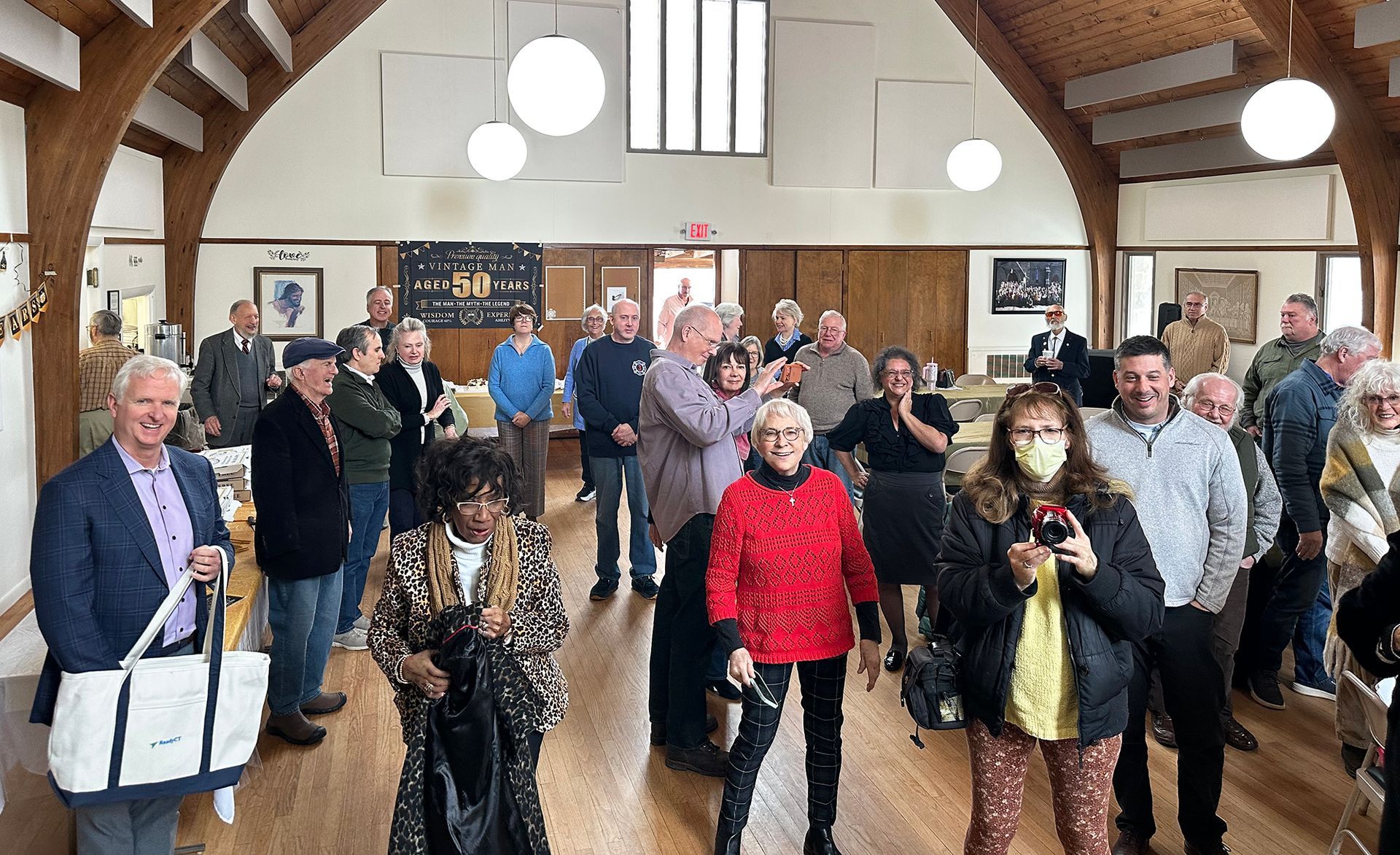 A large group of parishioners stands inside the Parish Hall following a special gathering.  