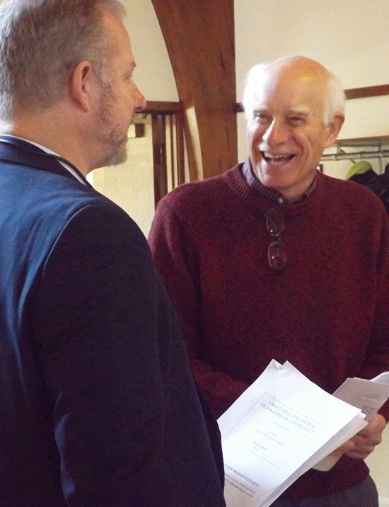 Two male parishioners chat together, laughing and smiling warmly.