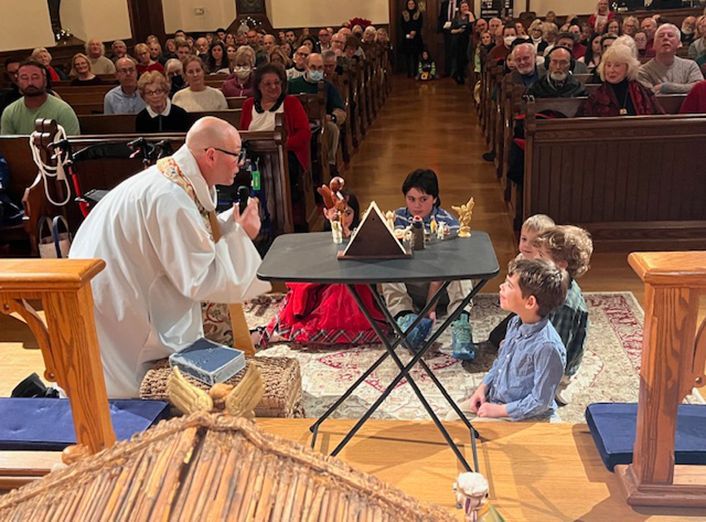 The minister crouches to address a small group of children on the altar floor, w/parishioners seated in full pews behind them