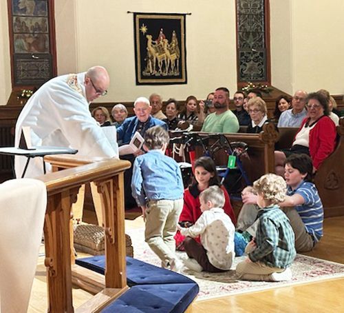Clergy addresses the congregation seated in pews & a small group of children sitting on the altar floor near communion rail